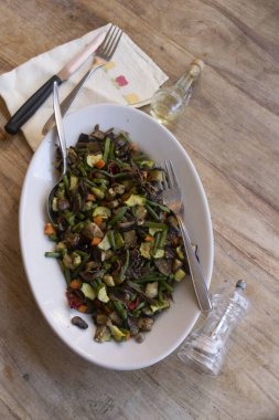 Sağlıklı vejetaryen kızartması karışık sebzeler, mantarlar, yeşil fasulyeler ve beyaz kasede servis edilen, ahşap masa çatallı, etsiz diyet.