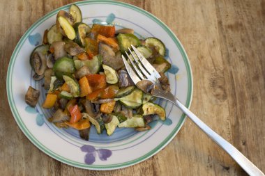 Renkli sotelenmiş sebze karışımı kabak biberli mantarlar ve besleyici vejetaryen öğle yemeği için çatalla dekoratif tabakta ya da ahşap masada akşam yemeği.