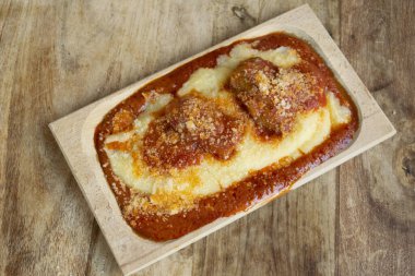 Üzerine zengin domates sosisi ve rendelenmiş peynir serpiştirilmiş domuz pirzolası serpiştirilmiş İtalyan kremalı polenta.