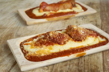 Üzerine zengin domates sosisi ve rendelenmiş peynir serpiştirilmiş domuz pirzolası serpiştirilmiş İtalyan kremalı polenta.