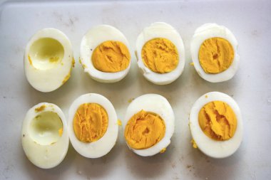 Beyaz bir zemin üzerinde ikiye bölünmüş haşlanmış yumurtaların üst görüntüsünde yumurta sarısı eksik. Düşük kolesterolü ya da yüksek protein uygunluğunu temsil ediyor.