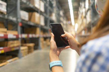 Depoda dokunmatik cep telefonu kullanan modern bir kadın. Cep telefonu tutan, cep telefonu sipariş eden, akıllı telefondan alışveriş yapan bir kız. yönetim hisseleri çevrimiçi hizmet sektörü kavramı.