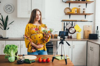 Genç, güzel, hamile kız blogcu akıllı telefon kamerasıyla salata tarifinin videosunu çekiyor. Sağlıklı beslenme kavramı. Tonlama.