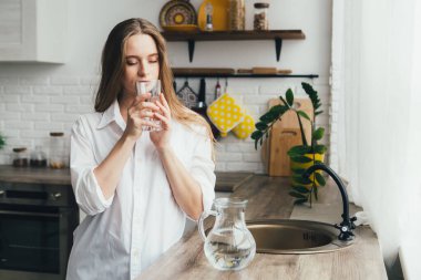 Genç ve güzel hamile kız mutfakta temiz su içiyor. Sağlıklı yaşam tarzı kavramı. Tonlama.