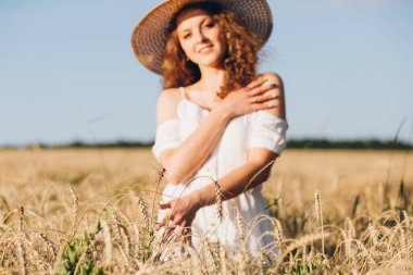 Uzun kıvırcık saçlı genç bir kız yazın gün batımında buğday tarlasında poz veriyor. Şapkalı kız. Tonlama.