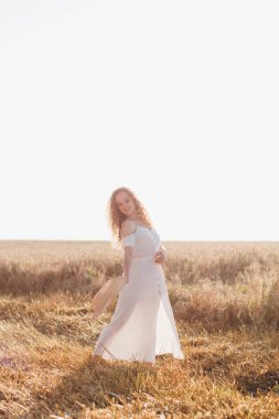 Uzun kıvırcık saçlı genç bir kız yazın gün batımında buğday tarlasında poz veriyor. Şapkalı kız. Tonlama.