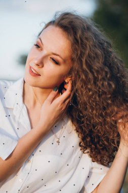 Uzun kıvırcık saçlı genç bir kız yazın gün batımında buğday tarlasında poz veriyor. Tonlama.