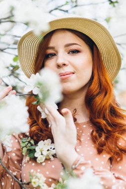 Genç, güzel, kızıl saçlı kız bahar çiçekli bir elma bahçesinde yürüyor. Boyama.