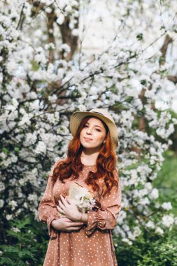 Genç, güzel, kızıl saçlı kız bahar çiçekli bir elma bahçesinde yürüyor. Boyama.