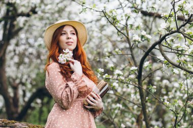Genç, güzel, kızıl saçlı kız bahar çiçekli bir elma bahçesinde yürüyor. Boyama.