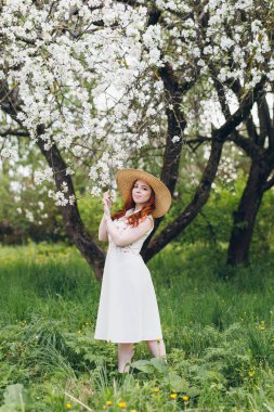 Genç, güzel, kızıl saçlı kız bahar çiçekli bir elma bahçesinde yürüyor. Boyama.