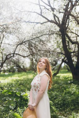 Genç, güzel, kızıl saçlı kız bahar çiçekli bir elma bahçesinde yürüyor. Boyama.