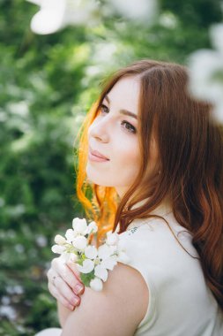 Genç, güzel, kızıl saçlı kız bahar çiçekli bir elma bahçesinde yürüyor. Boyama.