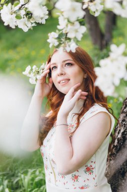 Genç, güzel, kızıl saçlı kız bahar çiçekli bir elma bahçesinde yürüyor. Boyama.