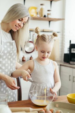 Sevimli küçük kız, annenin mutfakta kurabiye pişirmesine yardım ediyor. Mutlu bir aile. Tonlama.
