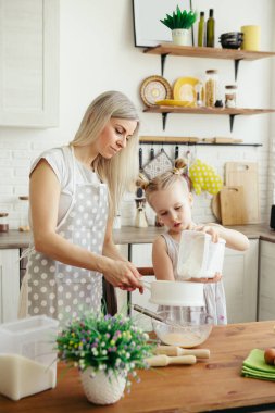 Sevimli küçük kız, annenin mutfakta kurabiye pişirmesine yardım ediyor. Mutlu bir aile. Tonlama.