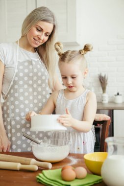 Sevimli küçük kız, annenin mutfakta kurabiye pişirmesine yardım ediyor. Mutlu bir aile. Tonlama.