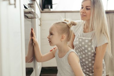 Sevimli küçük kız, annenin mutfakta kurabiye pişirmesine yardım ediyor. Mutlu bir aile. Tonlama.
