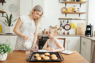 Şirin küçük kız ve anne mutfakta taze pişmiş kurabiye ve süt yiyorlar. Mutlu bir aile. Tonlama.