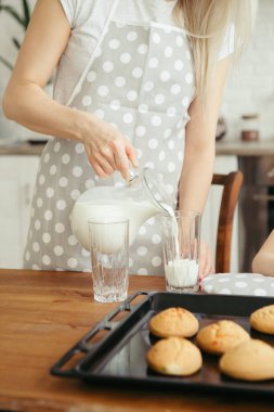 Şirin küçük kız ve anne mutfakta taze pişmiş kurabiye ve süt yiyorlar. Mutlu bir aile. Tonlama.