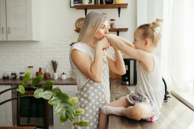 Genç ve güzel bir kadın küçük tatlı kızını kucaklıyor ve öpüyor. Tonlama.
