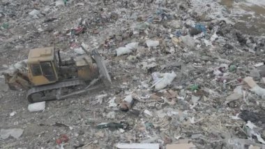Buldozer traktörü şehir çöplüğündeki bir dağdan çöp atıyor.