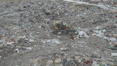 Buldozer traktörü şehir çöplüğündeki bir dağdan çöp atıyor.