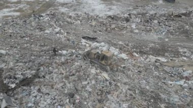 Buldozer traktörü şehir çöplüğündeki bir dağdan çöp atıyor.