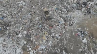 Buldozer traktörü şehir çöplüğündeki bir dağdan çöp atıyor.