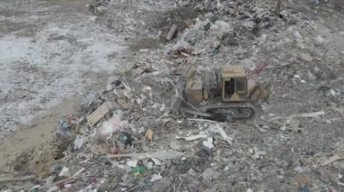 Buldozer traktörü şehir çöplüğündeki bir dağdan çöp atıyor.