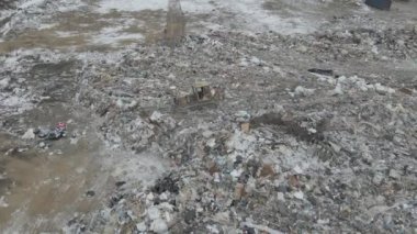 Buldozer traktörü şehir çöplüğündeki bir dağdan çöp atıyor.