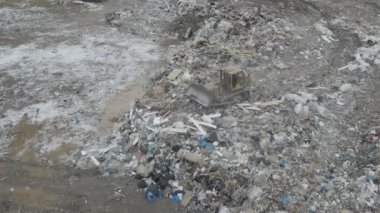 Buldozer traktörü şehir çöplüğündeki bir dağdan çöp atıyor.