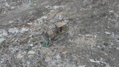 Buldozer traktörü şehir çöplüğündeki bir dağdan çöp atıyor.