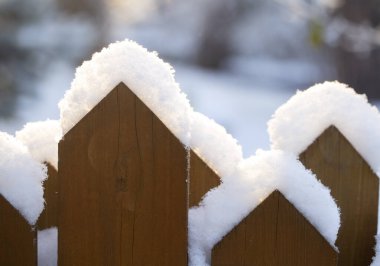 Kışın güneş ışığında karla kaplı çitler.