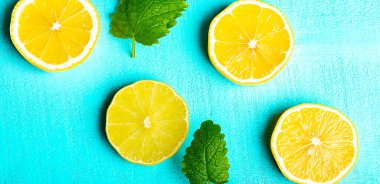 Masanın turkuaz yüzeyinde naneli ve buzlu dilimlenmiş limon, yakın plan.