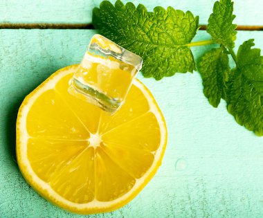 Masanın turkuaz yüzeyinde naneli ve buzlu dilimlenmiş limon, yakın plan.