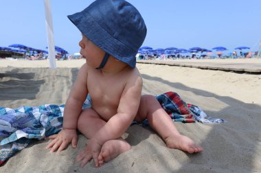 Bebeğimiz kumsalda kot şapkalı bir havluyla oynuyor.