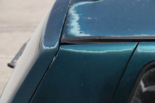 Faded car paint - peeling paint surface in a 15 year old compact green car. Sun worn paint.