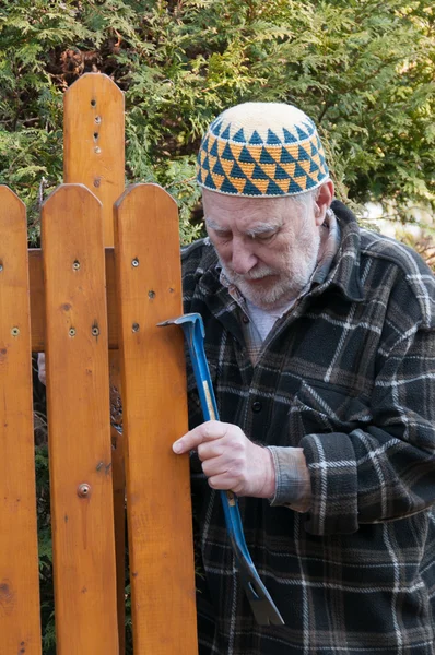 Старик ремонтирует ворота — стоковое фото
