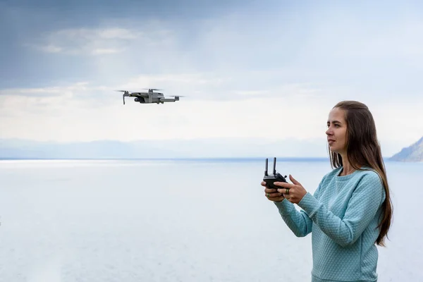 Beautiful young woman having fun with a mini drone outdoors. The girl stands against water background