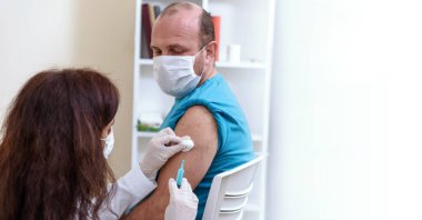 Eldivenli doktor elinde şırıngayla hastaya tıbbi maske takıyor..