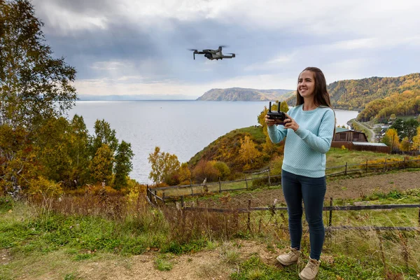 Beautiful young woman having fun with a mini drone outdoors. The girl stands against the autumn forest background — Stock Photo, Image