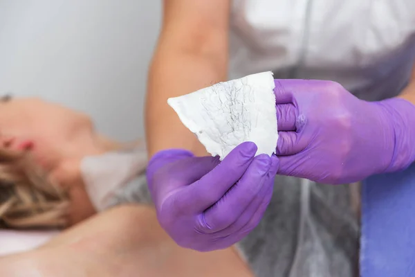 Hand with purple gloves are holding used wax stripes with removed hair. Depilation skin in spa salon — Stock Photo, Image