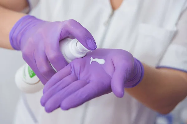 Cosmetologist squeezing out a tube of cream on her hand with gloves