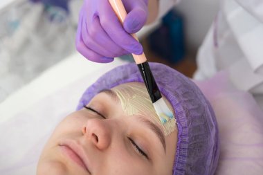 Güzellik salonunda, güzellik uzmanı genç bir kızın yüzüne yeşil kilden bir maske takar. Günlük cilt bakımı.