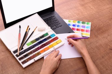 Çevrimiçi çizim sınıfı kapağı konsepti, dizüstü bilgisayar, kağıt, boyalar ve fırçalar ahşap ofis masasında. Çevrimiçi eğitim