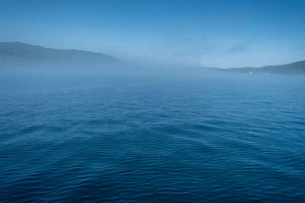 Baikalsee in der Nähe des Dorfes Port Baikal, Russland. Sonniger Tagesblick auf das hohe Ufer und klares Seewasser mit Nebel — Stockfoto