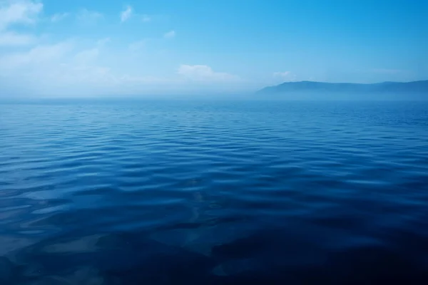 Waves on surface of water with cloudy sky and mountain. Copy space — Stock Photo, Image