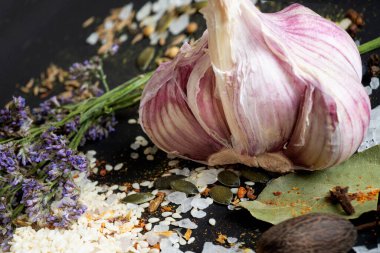 Baharatların etrafında taze sarımsak ve siyah arka planda deniz tuzu. baharatlar, renkli doğal yemek katkı maddeleri. Sağlıklı gıda konsepti. Kapat.