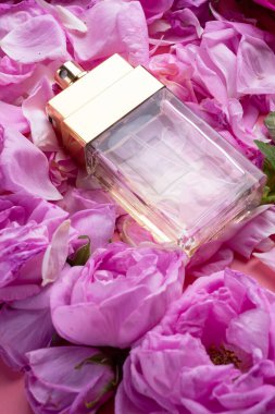 Etrafında pembe arka planda güller olan bir şişe parfüm var. romantik ve güzellik konsepti 